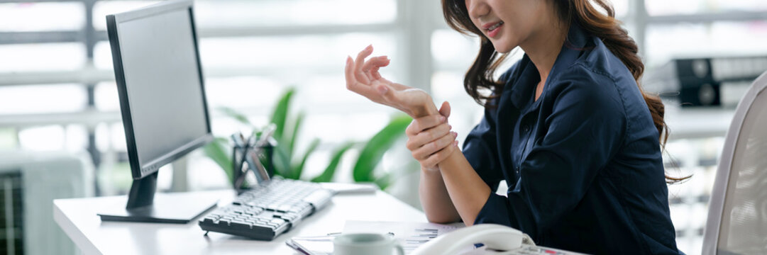 Woman holds hand in pain while working, office syndrome