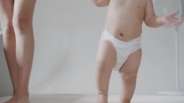 Close up of cute baby feet taking first steps on mat with parent support.