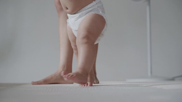 Close up of cute baby feet taking first steps on mat with parent support.