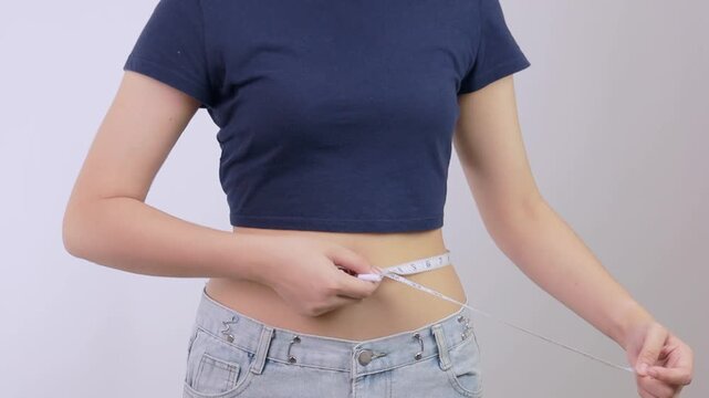 Proud happy woman measures slim waist with white tape showing successful diet and fitness journey for healthy weight loss transformation goal