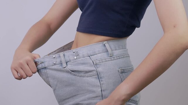 Proud woman shares successful weight loss transformation wearing oversized blue denim pants showcasing her confident slim fit waist