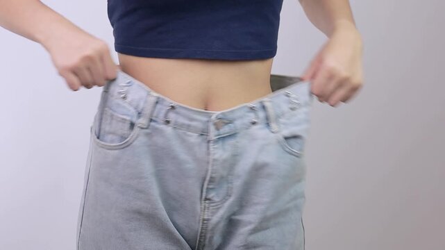 Proud woman shows weight loss transformation wearing loose denim pant with oversized waist revealing slim belly after successful healthy diet