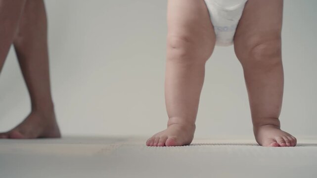 Close up of cute baby feet taking first steps on mat with parent support.