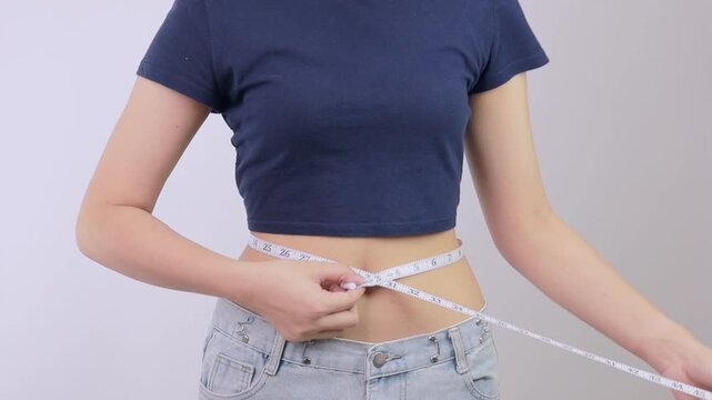 Proud young woman celebrating successful healthy body weight loss transformation progress, holding tape measure around slim waist with raised fist