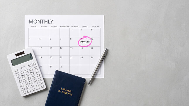 Flat lay of a monthly calendar with payday marked, featuring a calculator and savings bankbook for personal finance management.