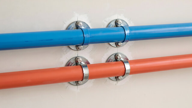 Blue and red water pipes mounted on a white wall with metal clamps