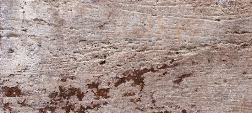 Old weathered pink sandstone wall texture with rough peeling surface and graffiti