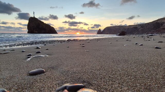Golden sunset illuminates ocean waves crashing against a rocky volcanic shore. Static low angle ground level perspective shot.