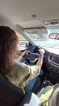 Young woman driving car along suburban road while adjusting visor. Side profile shot with static camera orientation.