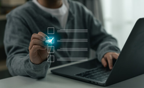 Person checking a box on a virtual digital checklist interface while working on a laptop, business concepts of tasks management and quality control.