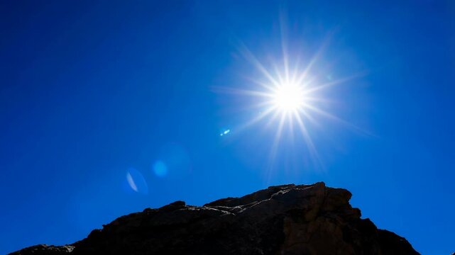 Bright sun shining over rocky mountain peak with clear blue sky on a sunny day