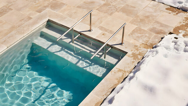Swimming pool with metal stairs and stone patio covered in winter snow