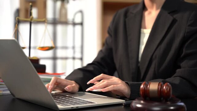 Justice at Work: A focused legal professional types on a laptop in an office setting, with scales of justice and a gavel nearby, symbolizing the pursuit of fairness and legal expertise.