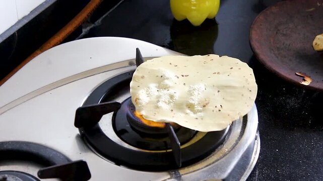 Vertical close-up of hand roasting papad over open gas flame in Indian kitchen. Ideal for recipe tutorials, traditional cooking, food blogs, restaurant, and culinary content.