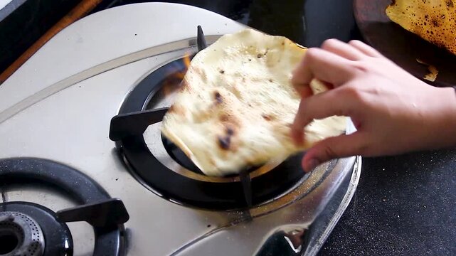 Papad held over open gas flame until crisp, close-up shot in Indian kitchen. Ideal for food content, cooking tutorials, and authentic culinary B-roll.