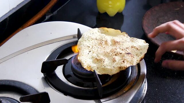 Vertical close-up of papad puffing and roasting over open gas flame in Indian home kitchen. Ideal for recipe tutorials, traditional cooking, food blogs, and culinary content.