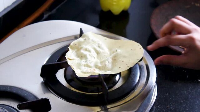 Vertical close-up of papad roasting directly over gas flame in an Indian kitchen. Perfect for cooking tutorials, Indian cuisine, recipe videos, food blogs, and traditional meal preparation.