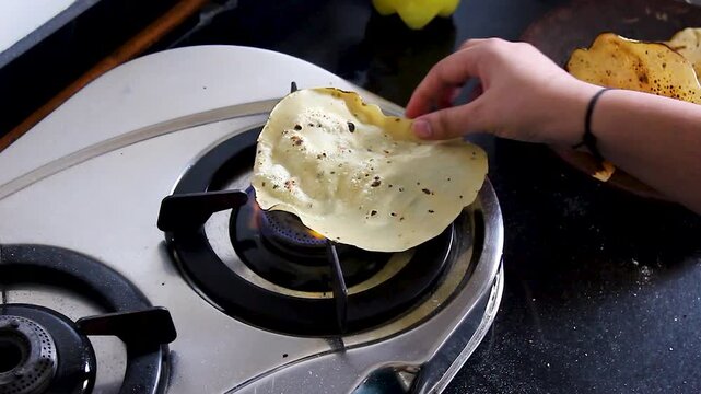 Hand roasting crispy papad directly over gas stove flame in Indian kitchen. Ideal for food content, culinary tutorials, and authentic home-cooking footage.