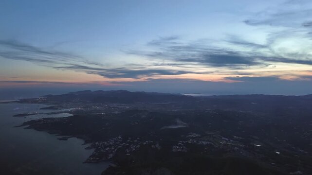 Aerial airplane cockpit view of Ibiza island and city captured at twilight from an airplane, wih some clouds in a purple sky and a calm Mediterranean Sea.