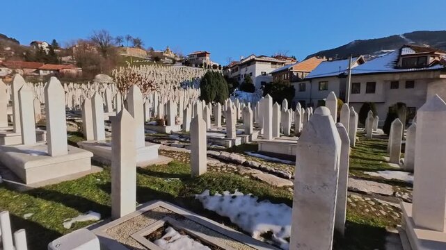 Smooth tracking or gimbal shot moving forward through rows of traditional Islamic white marble tombstones (Nisani) at Kovači Martyr Cemetery