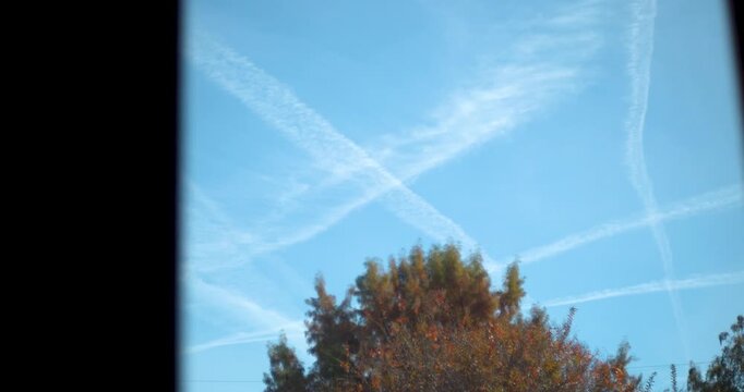 Multiple white jet contrails crisscross in a bright blue sky over orange autumn foliage in New Orleans, Louisiana. Authentic cinematic look for environmental or travel themes.