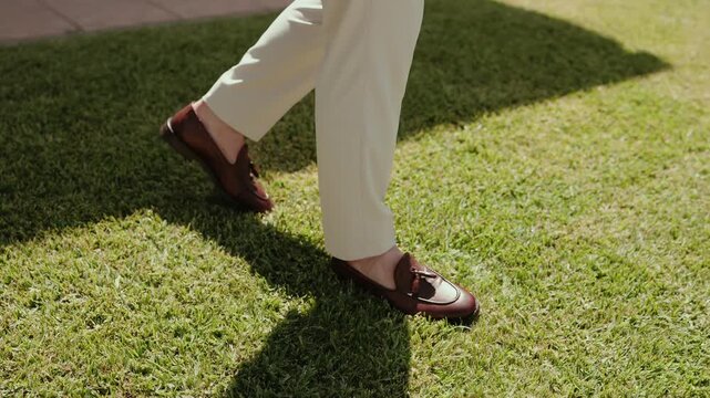 Legs and brown leather tassel loafers stand on grass edge near stone paved patio outdoors