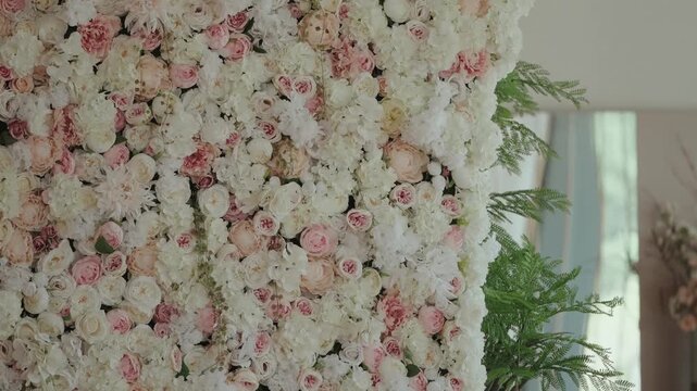 Lush flower wall of roses and peonies in white and blush pink beside greenery indoors