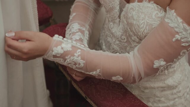 Description:
Woman in white lace wedding dress adjusts sheer sleeve with gold ring visible on hand