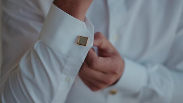 Hand fixes gold cufflink on crisp white shirt collar during formal wear preparation