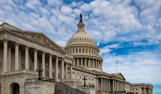 Capitol in USA skyline background. Federal Capitol on blue sky in Washington DC. Patriotic Capitol with American flag in daytime. Iconic Capitol monument on cloudy sky.