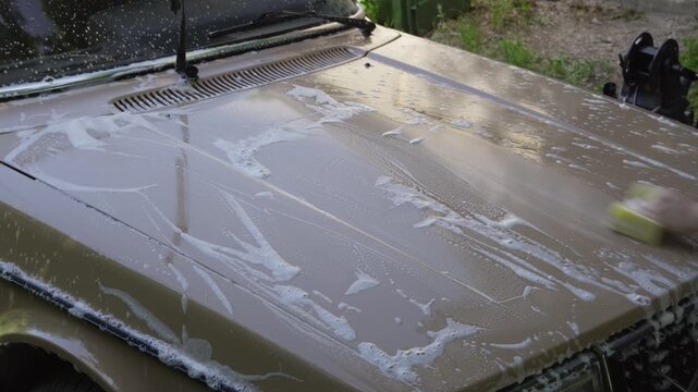 A person hand washes a vintage car hood with soapy water at home. Ideal for classic car restoration, car care, detailing and automotive lifestyle content.