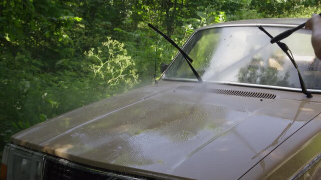 A man washes a classic car with a pressure washer outdoors. Ideal for car cleaning, auto detailing, vehicle restoration and automotive lifestyle content.