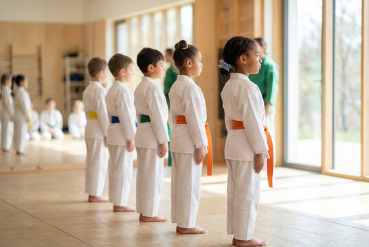 Row of diverse children in white uniforms standing in line during martial arts training class