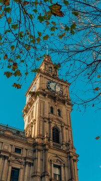 Historic stone clock tower against clear blue sky. Gothic architectural landmark with intricate masonry details and autumn foliage.