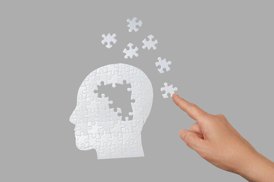 A hand positions a puzzle piece into a human head silhouette design
