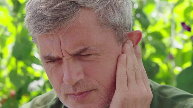 Middle-aged man suffering from severe earache outdoors, close-up