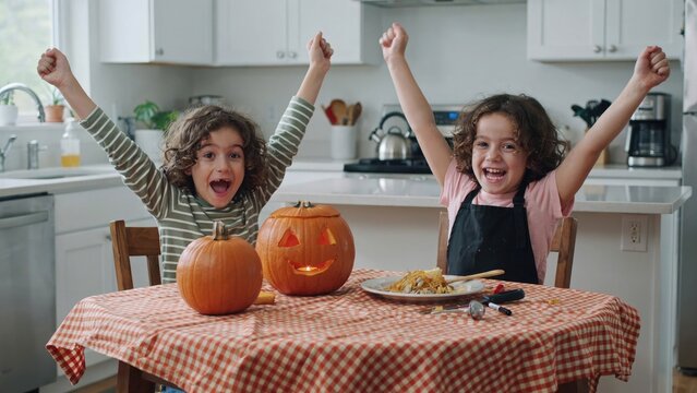 Excited twin children celebrating jack o' lantern carving in home kitchen