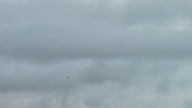 Small helicopter flies across grey cloudy sky over Torremolinos on hazy overcast day