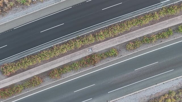 Cars travel opposite directions on divided road separated by median with shrubs from above