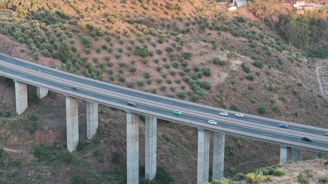 Cars drive across tall concrete viaduct spanning dry hillside terrain in Malaga Spain