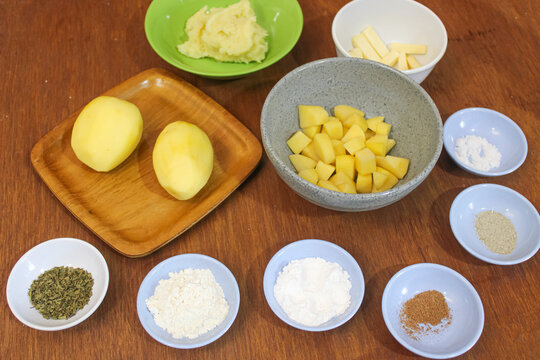 Fresh raw potato ingredients and culinary spices in bowls on wooden table