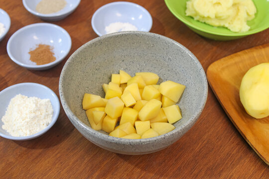 Fresh raw diced yellow potato cubes in ceramic bowl on kitchen wooden table