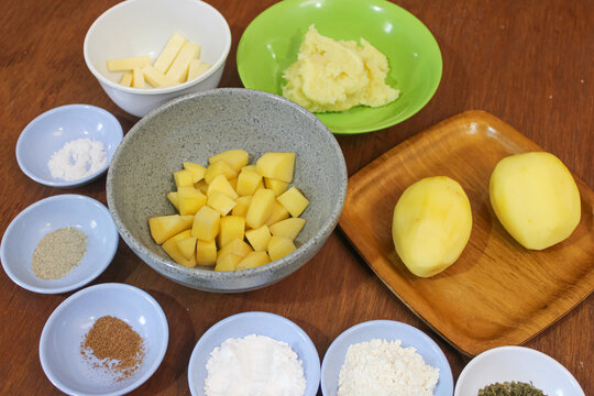 Fresh raw diced potatoes and baking ingredients in bowls on wooden table