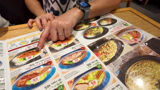 Person Pointing at Ramen Dishes on Restaurant Menu
