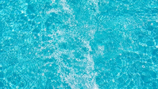A dynamic aerial shot of splashing pool water with white foam bubbles and turquoise caustics.