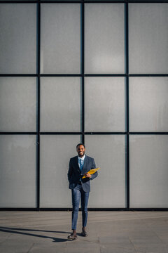Black businessman holding folder smiling outdoors urban setting