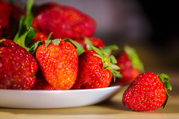 Side View of White Plate with Pile of Fresh Red Strawberries and Single Berry on Wood © Екатерина Переславце