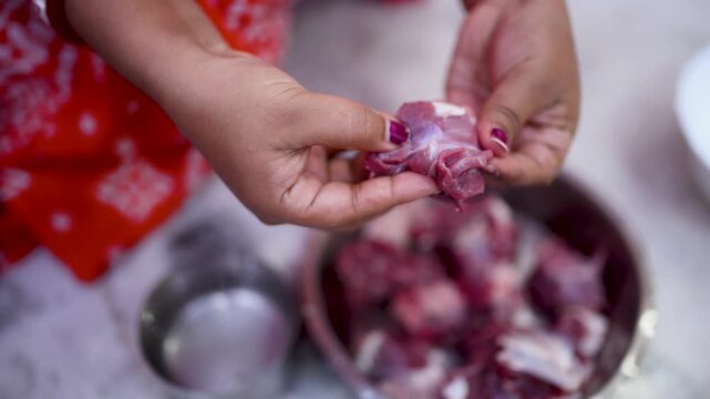 A married Indian woman hygienically cleans fresh red mutton pieces by hand in a clean kitchen, emphasizing food safety, cleanliness, traditional cooking, and careful meat preparation. 