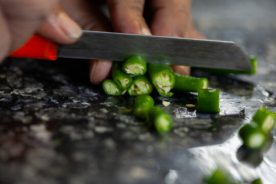 Indian female hand slicing fresh green chili peppers