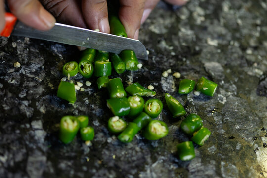 Indian female hand slicing fresh green chili peppers